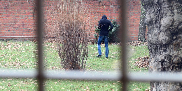 Mann in schwarzer Kaputze läuft hinter Gittern durch einen Garten