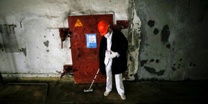 Ein Mann mit einem roten Bauhelm in einem geschlossenen Raum, hinter ihm eine Tür