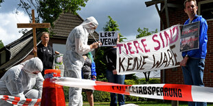 Tierschützer halten Plakate und ein Kreuz in die Luft.