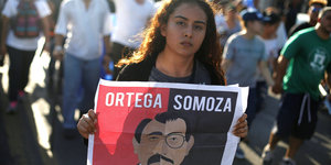 Eine junge Frau hält ein Plakat in den Händen, auf dem Ortega mit Somoza verglichen wird