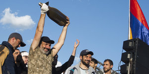 Ein Mann hält eine Riesenflasche in die Höhe, umstanden von anderen Männern, rechts im Bildrand die armenische Fahne