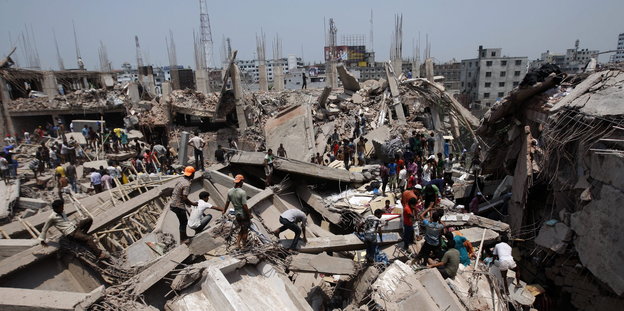 Ein eingestürztes Gebäude, mehrere Menschen stehen auf den Trümmern