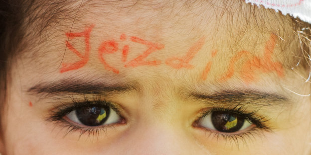 Auf die Stirn eines Kindes ist das Wort "jesidisch" gemalt