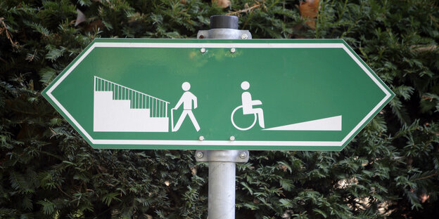 Ein Schild, links ist jemand vor einer Treppe, rechts ist jemand vor einer Rollstuhlrampe abgebildet, Treppe und Rampe führen in unterschiedliche Richtungen