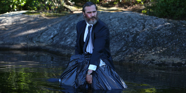 Ein Mann steht im Wasser und hält einen Plastiksack