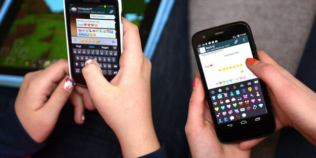 Zwei Teenager halten Smartphones in den Händen, auf denen sie den Messengerdienst WhatsApp benutzen