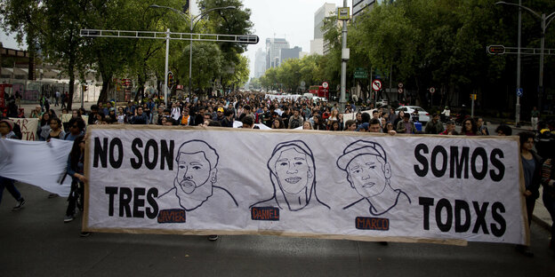 Menschen laufen auf der Straße und tragen ein Transparent mit der Zeichnung dreier Gesichter