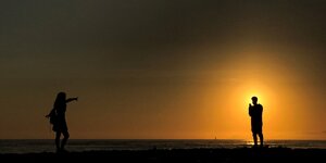 Mann und Frau am Strand bei Sonnenaufgang