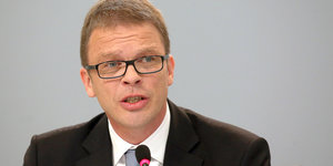 Der Chef der Deutschen Bank, Christian Sewing, sitzt mit Anzug und Krawatte hinter einem Mikrofon