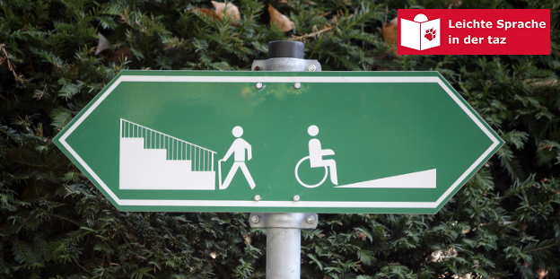 Ein Schild, links ist jemand vor einer Treppe, rechts ist jemand vor einer Rollstuhlrampe abgebildet, Treppe und Rampe führen in unterschiedliche Richtungen