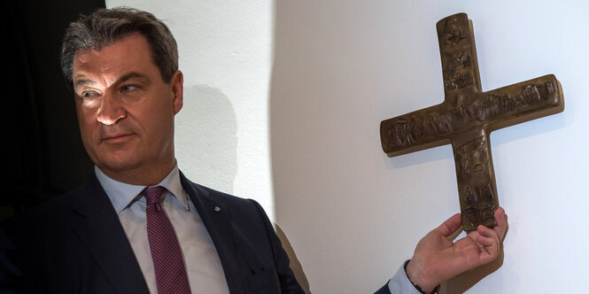 Markus Söder berührt mit der Hand ein Kreuz an der Wand