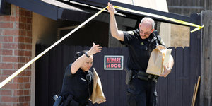 Zwei Polizisten tragen Beutel aus einem Haus