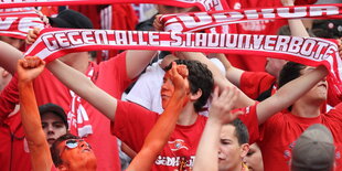 Menschen in roter Kleidung. Einer hält einen Schal mit der Aufschrift „Gegen alle Stadionverbote"