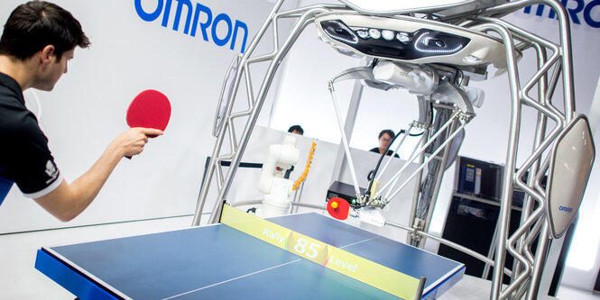 Ein Mensch spielt Tischtennis gegen einen Roboter.