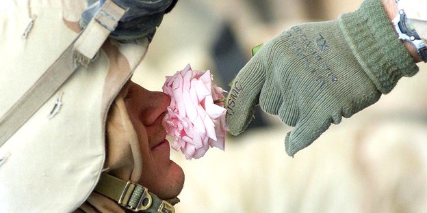 Eine Hand hält einem Soldaten eine rosafarbene Blume unter die Nase