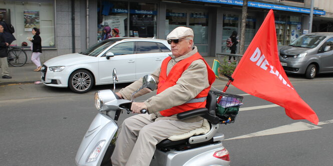 Ein Mann fährt mit dem Elektroroller und einer Flagge der Linkspartei