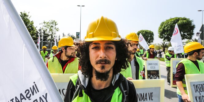 Mann mit Bauhelm, hinter ihm Demonstrierende