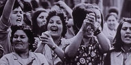 Mehrere Frauen stehen in einer Gruppe lachen und heben die Hände
