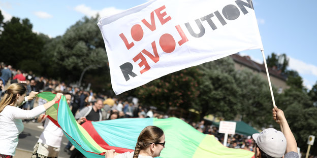 Menschen vor ein paar Bäumen mit einer Fahne mit der Aufschrift "Love Revolution"