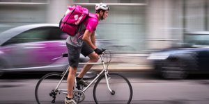 Ein Foodora-Kurier mit pinkem Rucksack fährt Fahrrad