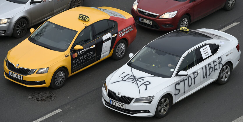 Ein Auto, das mit dem Schriftzug „stop uber" versehen ist, steht auf der Fahrbahn neben einem Taxi