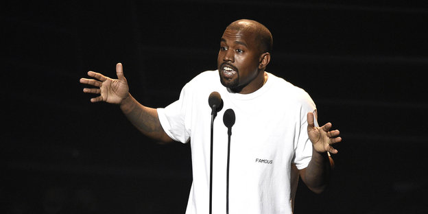 Kanye West in weißem Hemd spricht ins Mikrophon und gestikuliert dabei
