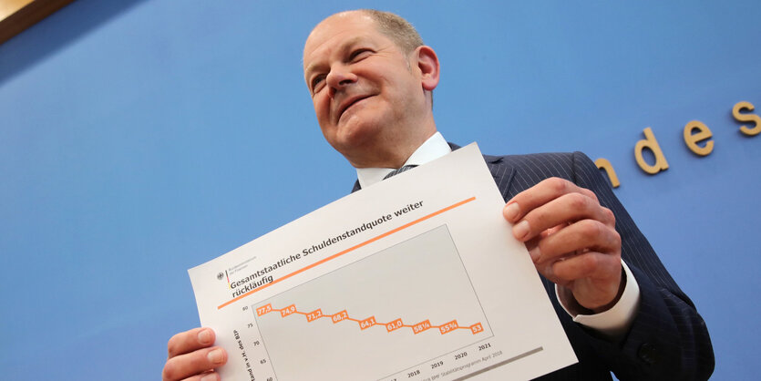 Olaf Scholz hält ein Papier in der Hand und lächelt