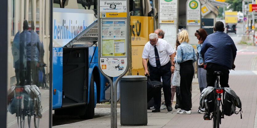 Ein Radfahrer fährt auf einem Radweg, auf dem Leute stehen, die in einen Bus einsteigen wollen.