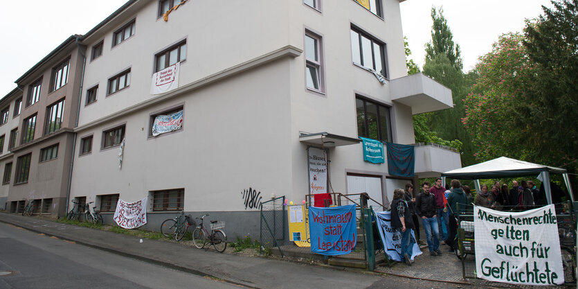 Vor einem Haus hängen Plakate und Menschen stehen vor dem Eingang.