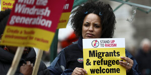Eine schwarze Frau hält ein gelbes Schild auf dem steht: Migrants and refugees welcome here