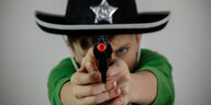 Ein Junge im Sherrifshut zielt mit einer Spielzeugpistole in die Kamera