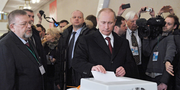 Putin steht an einer Wahlurne und gibt seinen Stimmzettel ab