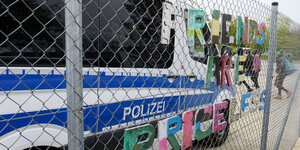 Ein großes weiß-blaues Polizeiauto steht vor einem Zaun