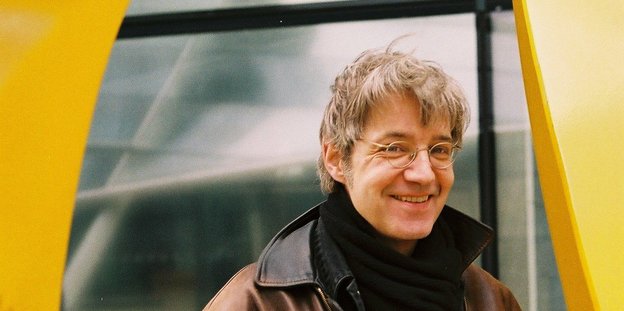 Ein lächelnder Mann mit grauen Haaren und runder Brille.