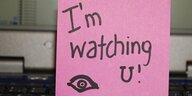 In einer Computertastatur steckt ein Zettel mit der Aufschrift: "I'm watching you".