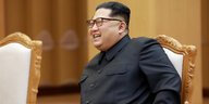 Kim Jong Un sitzt auf einem Stuhl und lacht