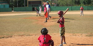 Kinder spielen auf einem spärlich mit Gras bewachsenen Platz Baseball