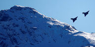 Zwei Kampfjets umfliegen eine Bergspitze.