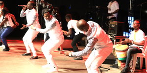 Mehrere Musiker in weißer Kleidung performen auf einer Bühne
