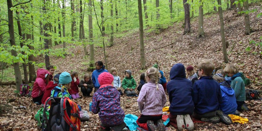 Kinder sitzen auf dem Waldboden im Kreis