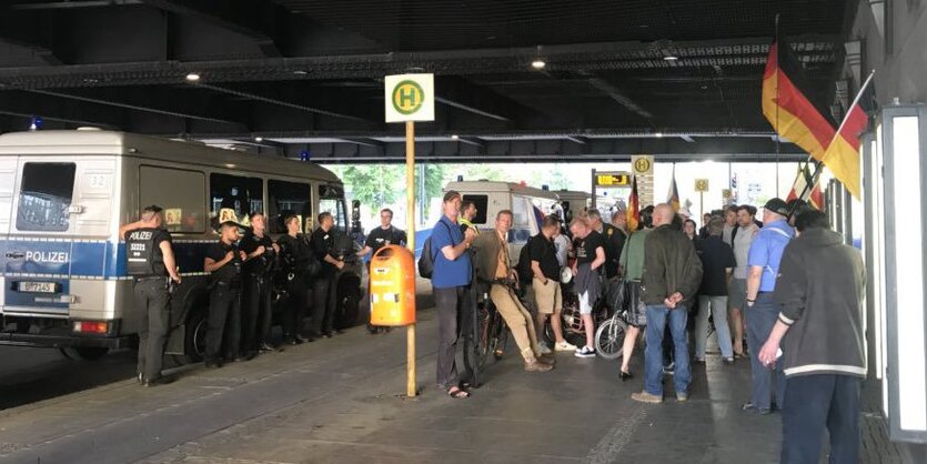 menschen mit Deutschlandfahnen unter einer Brücke, beäugt von der Polizei