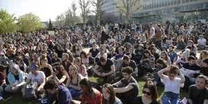 StudentInnen sitzen vor einer Universität auf dem Rasen