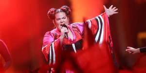 Eine Frau im bunten Kleid steht auf einer Bühne und singt