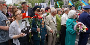 Menschen mit Blumen, Bildern Verstorbener und ein Mann in einer Uniform der Roten Armee