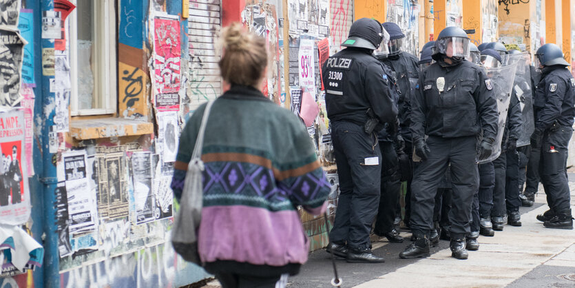 Eine Frau geht an einer Gruppe behelmter Polizisten vorbei