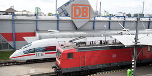 Ein ICE und eine Lokomotive vor einem Emblem der Deutschen Bahn