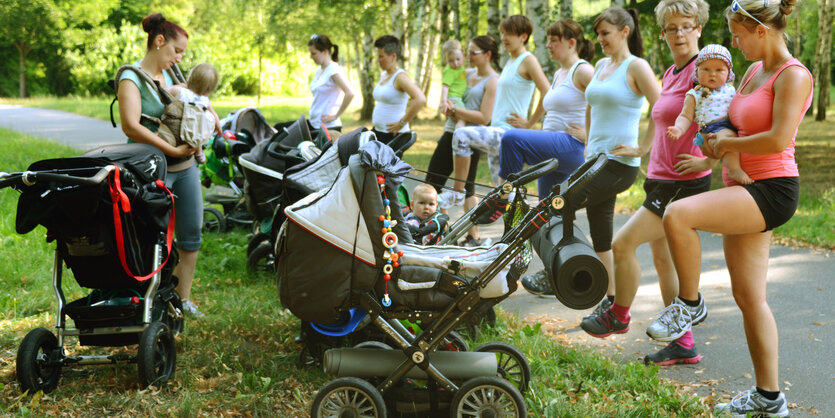 Mütter in Sportbekleidung, mit Babys auf dem Arm und mit Kinderwagen beim Sport im Park