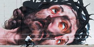 Eine Wandbemalung zeigt den Kopf von Jesus mit Dornenkrone, davor fährt jemand Fahrrad