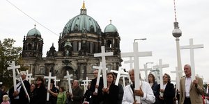 Mehrere Menschen laufen nebeneinander und halten weiße Kreuze hoch
