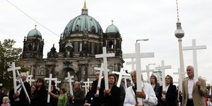 Mehrere Menschen laufen nebeneinander und halten weiße Kreuze hoch